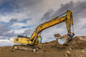 Yellow excavator digging under stormy cloudy sky