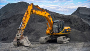 Excavator on gravel site, mountains behind