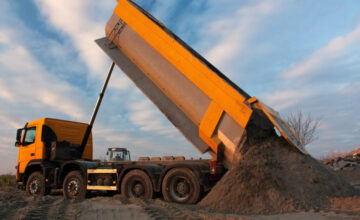 Dump truck unloading sand at sunset