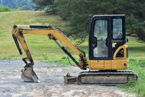 Excavator Types and Uses: Full Breakdown for Contractors 3 Compact yellow caterpillar excavator stands on gravel near grassy field. Construction equipment used for digging, earthworks, and small projects.