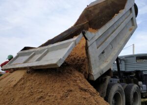 Dump truck unloading sand under cloudy sky.