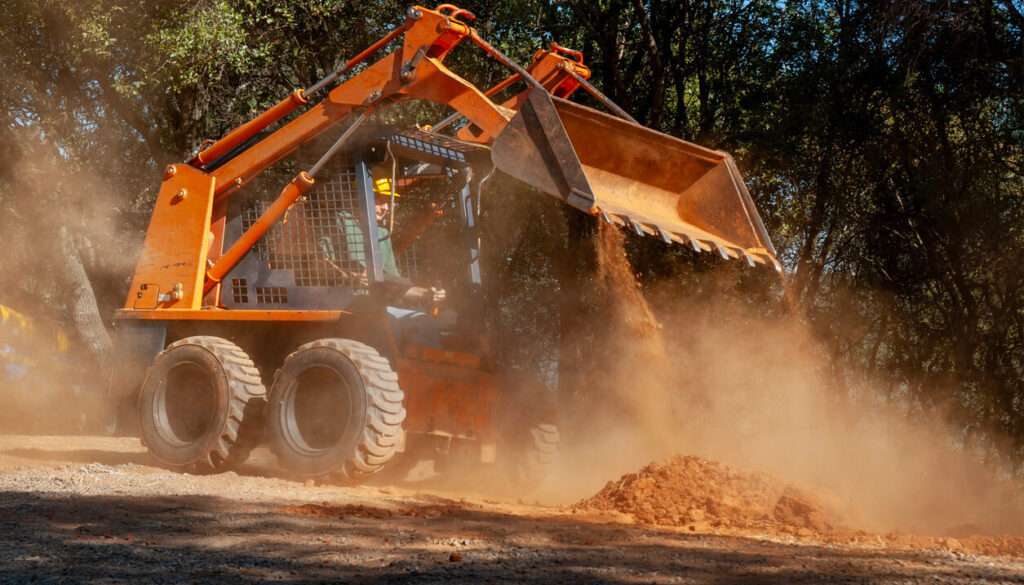 Skid steer moving dirt in sunlight.
