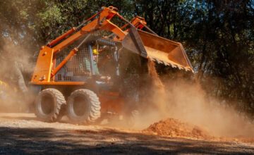 Skid steer moving dirt in sunlight.