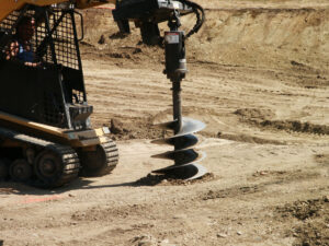 Top 5 Skid Steer Attachments for Contractors in 2026 3 Heavy machinery drilling into ground Auger attachment